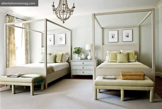 Bedroom with two queen-size canopy beds, light blue walls, and pale green accents on pillows and throws. A distressed wood chandelier hangs overhead.