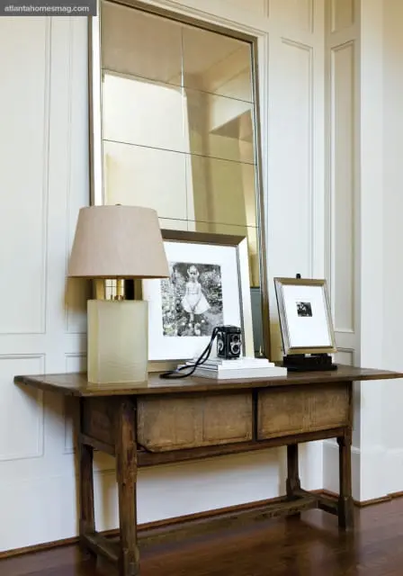 Wooden console table with two drawers topped with a lamp, framed black and white photos, and a vintage camera.