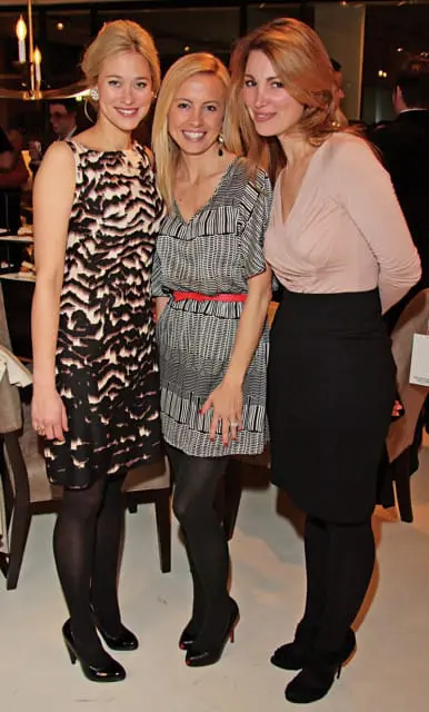 Three women posing for a photo. The woman on the left wears a black and white patterned dress. The woman in the middle wears a black and white striped dress with a red belt. The woman on the right wears a blush pink top and a black skirt.