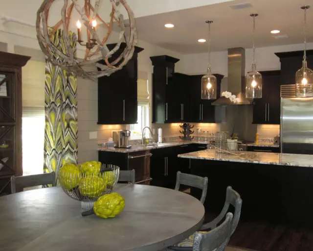 Dark wood kitchen with granite countertops, stainless steel appliances, and a large driftwood chandelier over a round metal dining table with yellow decorative artichokes.
