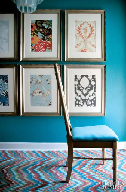 Turquoise walls adorned with framed art featuring floral and chinoiserie patterns, a gold-framed chair with a turquoise seat, and a colorful chevron rug.