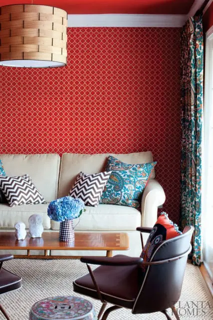 Living room with red quatrefoil wallpaper, a cream sofa with patterned pillows, a wooden coffee table with blue hydrangeas, and brown leather chairs.