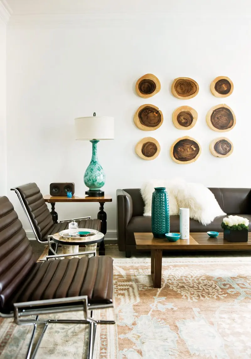 Living room with brown leather chairs, a dark brown sofa with a white fluffy pillow, a teal vase, and wall art made of wood slices.