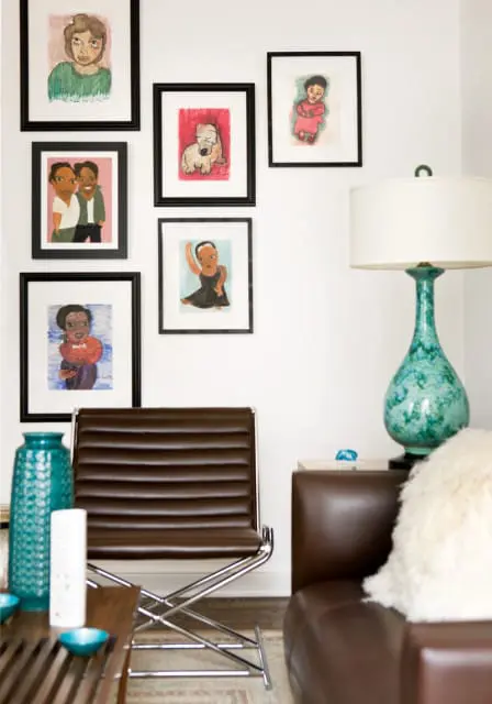 Living room with a gallery wall of framed children's drawings, a brown leather sling chair, a turquoise ceramic lamp, and a brown leather sofa with a fluffy white pillow.