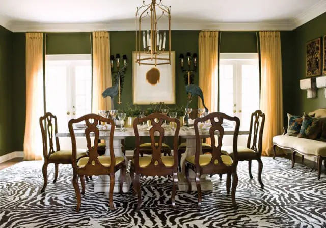 Dining room with dark green walls, a marble-topped dining table, ornate wooden chairs with yellow upholstery, and a zebra-print rug.