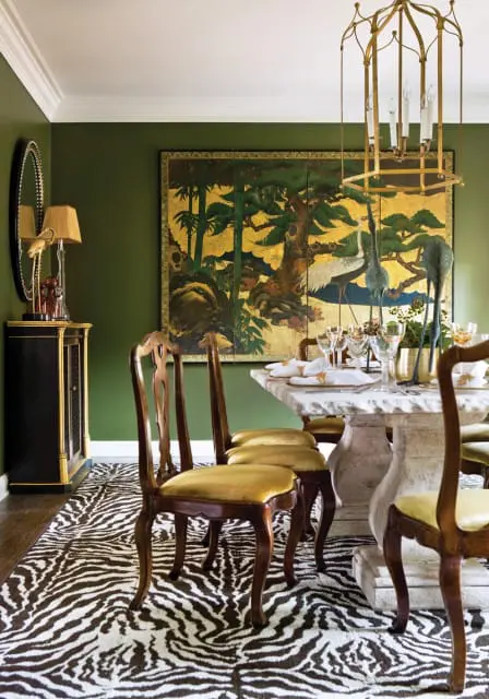 Dining room with olive green walls, a zebra print rug, and a stone pedestal dining table set for a meal.