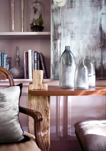 Shelf with books and decorative vases, including three glass bottles with frosted bases. A wooden chair with a patterned pillow is in the foreground.