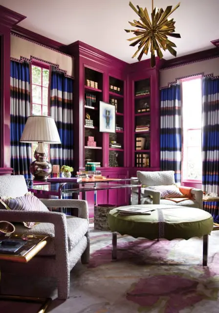 Study with magenta built-in bookshelves, striped curtains, glass desk, and upholstered chairs. A gold starburst chandelier hangs from the ceiling.