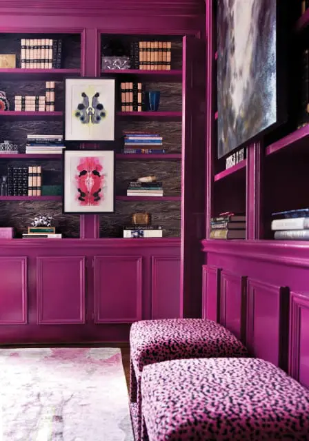 Library with magenta built-in bookshelves and cabinetry, featuring Rorschach test art, books, and leopard print ottomans.