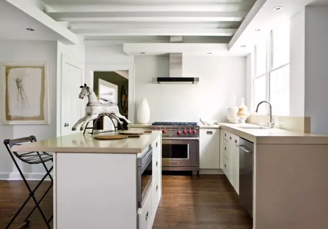 White kitchen with coffered ceiling, stainless steel range, light stone countertops, and a decorative rocking horse on the island.
