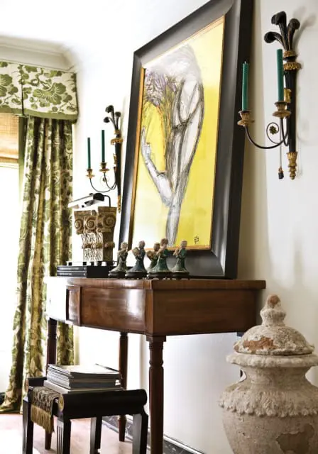 Entryway console table with a framed abstract painting, green floral curtains, and decorative figurines.