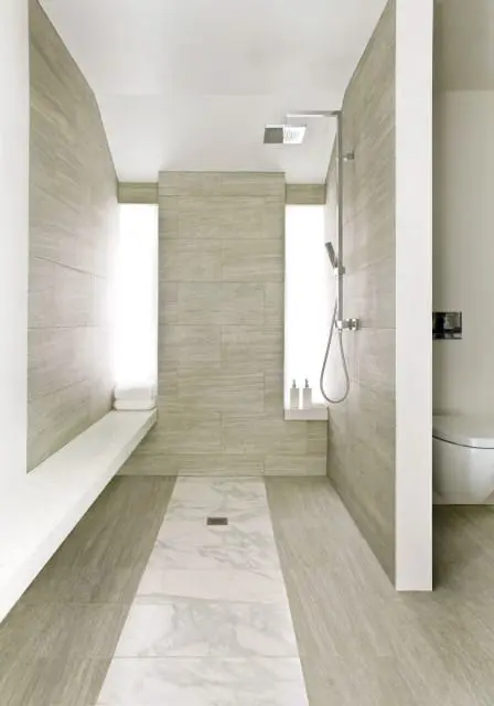 Modern bathroom with a walk-in shower featuring wood-look tile walls, a marble floor inlay, and a built-in bench. A toilet is visible to the right.