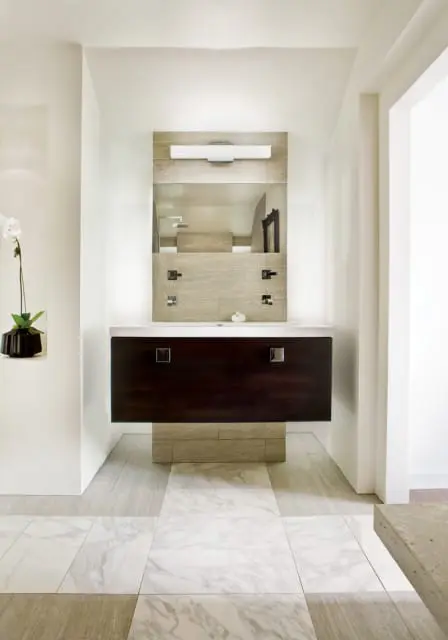 Modern bathroom vanity with dark wood drawers, white countertop, and wood-look tile backsplash. Marble and wood-look tile flooring.
