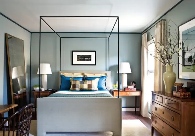 Bedroom with a light blue accent wall, a grey upholstered canopy bed, and dark wood furniture.