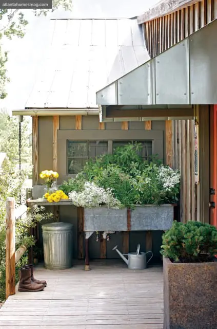 Rustic porch with galvanized wash tub overflowing with greenery, yellow flowers, boots, and watering can.