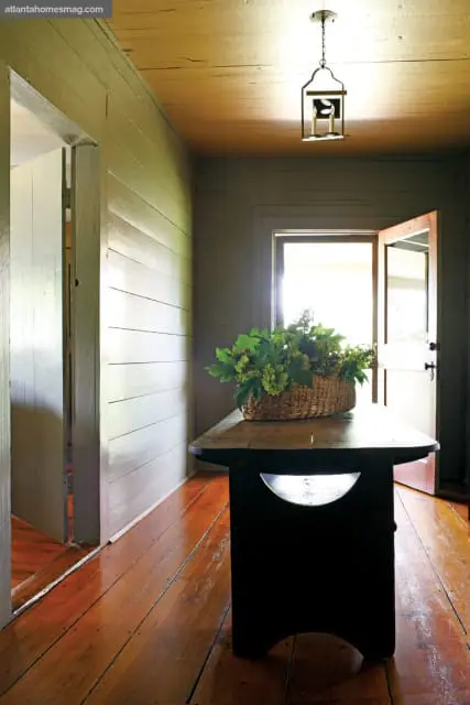 Hallway with wood plank walls and ceiling, a dark wooden table with a basket of greenery, and a lantern-style pendant light.