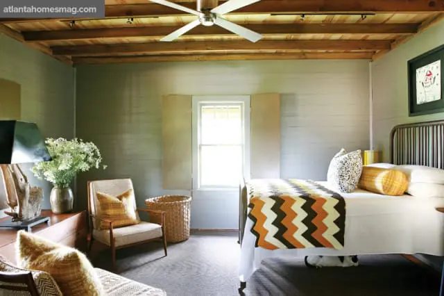 Bedroom with light gray horizontal wood plank walls, a white bed with a chevron blanket, a vintage metal bed frame, and a patterned armchair.