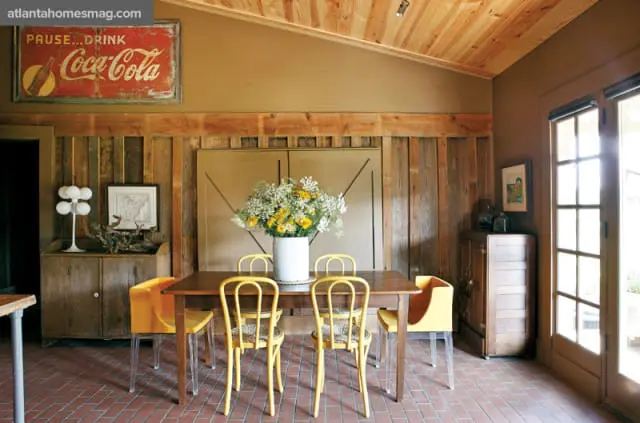 Dining room with a wooden table and chairs, a vintage Coca-Cola sign on the wall, and a large vase of flowers.