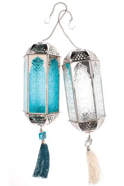 Pair of silver metal lanterns with embossed glass panels in aqua and clear, hanging from chains with tassels.