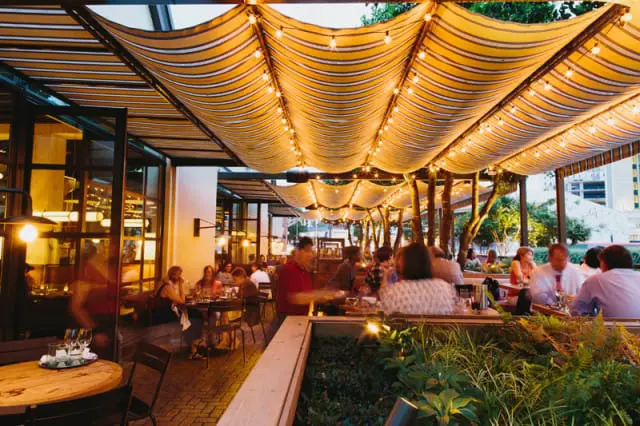 Outdoor dining area with striped awnings, string lights, and people dining at tables.