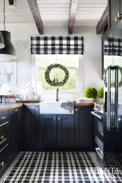 Black kitchen with white herringbone tile backsplash, farmhouse sink, wood countertops, and a black and white buffalo check rug.