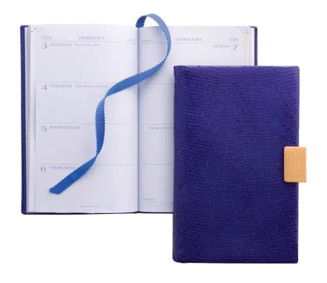 Close-up of an open 2011 diary with a blue ribbon bookmark and a closed purple textured diary with a gold clasp