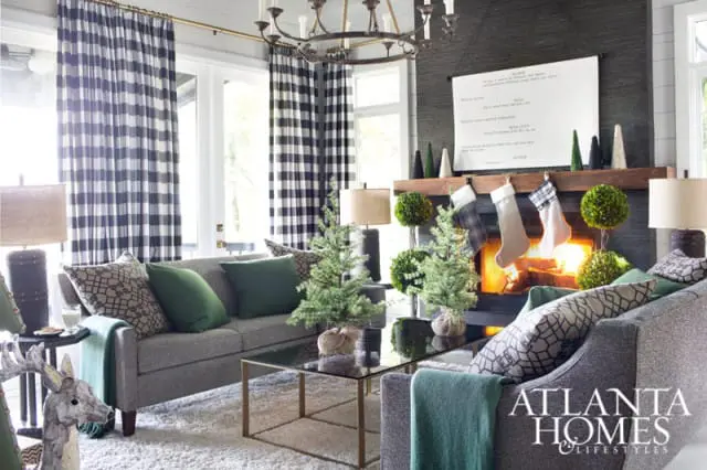 Living room with gray sofas, black and white checkered curtains, a fireplace with stockings, and Christmas trees.
