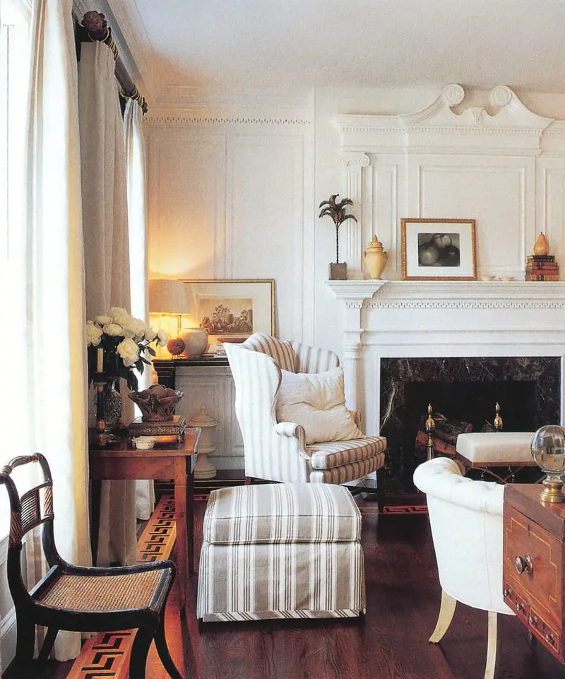 Living room with fireplace, wingback chair and ottoman upholstered in striped fabric, and a dark wood chair with cane seat.