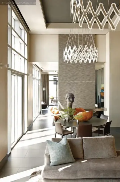Modern dining room with textured gray wall, round table with chairs, and a large sculptural chandelier. A sofa with a blue pillow is in the foreground.