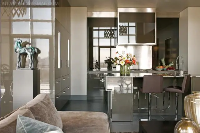 Modern kitchen with grey high-gloss cabinetry, stainless steel appliances, marble countertops, and a breakfast bar with leather stools.