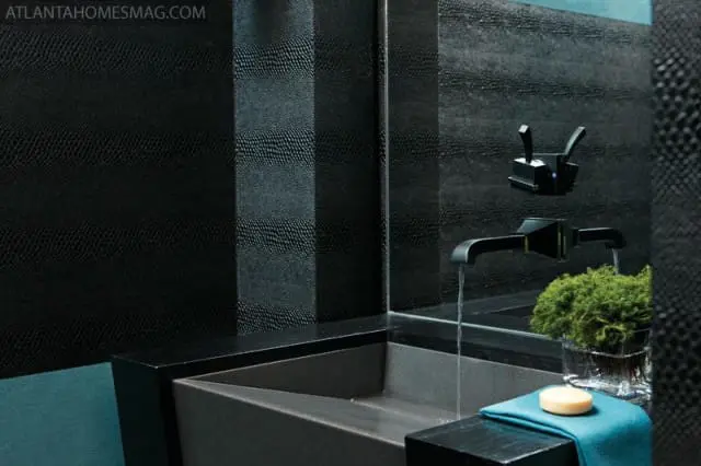 Modern black bathroom with textured snake-skin wallpaper, a dark gray concrete sink, and a black waterfall faucet with water flowing.