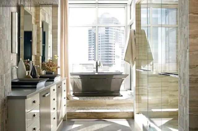 Modern bathroom with a freestanding stone tub, glass shower enclosure, and double vanity with marble countertops and stone tile accents.
