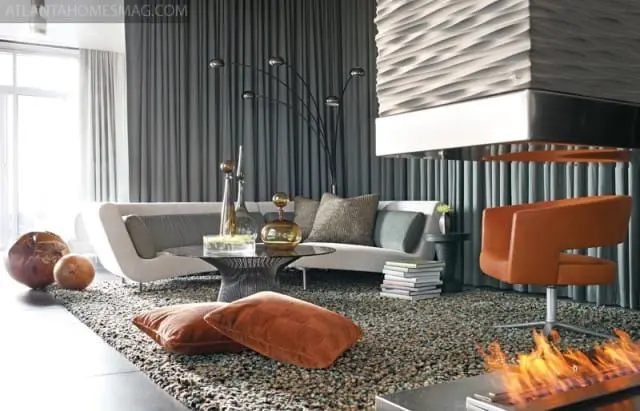 Modern living room with a white sofa, orange swivel chair, textured fireplace, and a multi-headed arc floor lamp against gray curtains.
