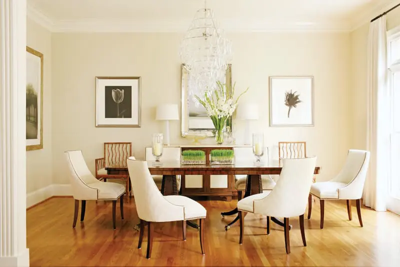 Dining room with a dark wood table, upholstered cream chairs, a crystal chandelier, and framed botanical prints on a cream wall.