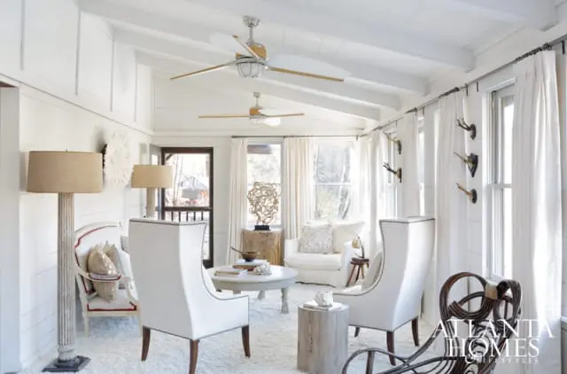 Sunroom with white shiplap walls and ceiling, two ceiling fans, white upholstered chairs, a round coffee table, and floor lamps. Antlers are mounted on the wall.