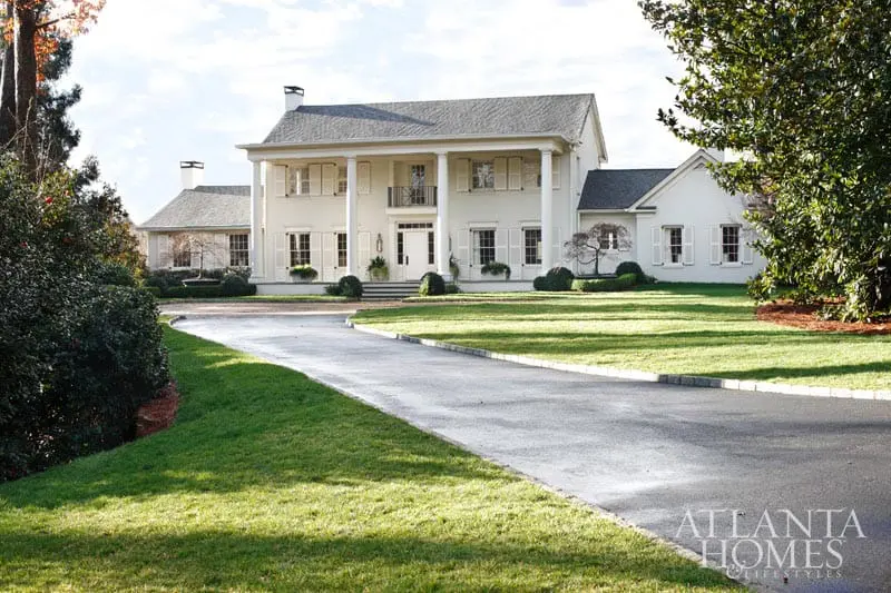 White neoclassical house with a grand portico supported by columns, shutters on windows, and a winding driveway leading to the entrance.