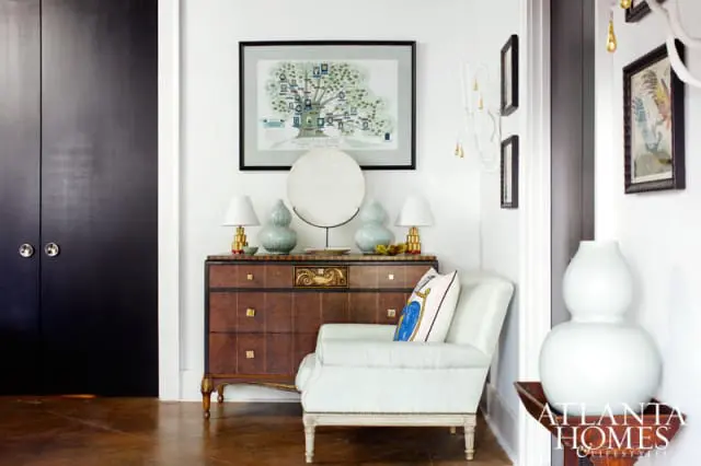 Entryway with dark wood double doors, a vintage dresser with decorative art and lamps, and a light blue armchair with a patterned pillow.