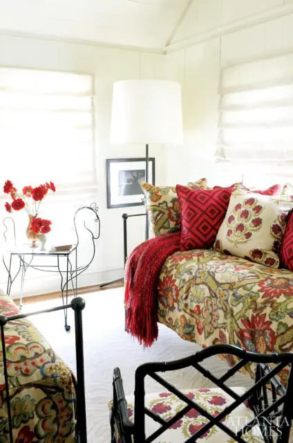 Bedroom with two daybeds upholstered in floral fabric, red knit throw, and patterned accent pillows. A black metal floor lamp stands behind the daybeds.
