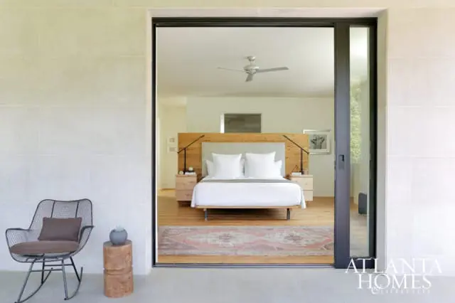 Bedroom with a king-size bed, light wood headboard, white bedding, and two nightstands, viewed through a sliding glass door.