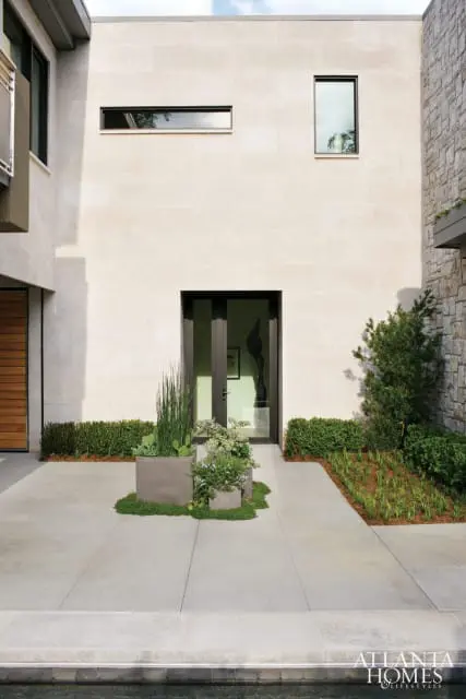 Modern home exterior with light stone facade, large glass double doors, and minimalist landscaping with planters.
