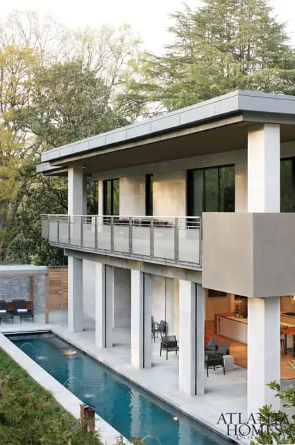 Modern concrete house with a long lap pool and balcony, surrounded by trees. Visible logo for Atlanta Homes & Lifestyles.