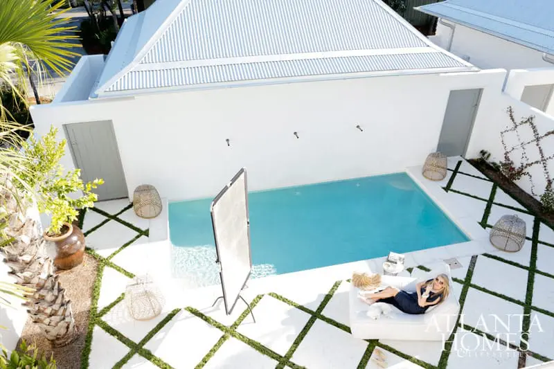 Aerial view of a modern white courtyard with a bright blue swimming pool, white lounge chair with a woman relaxing, and decorative woven baskets.