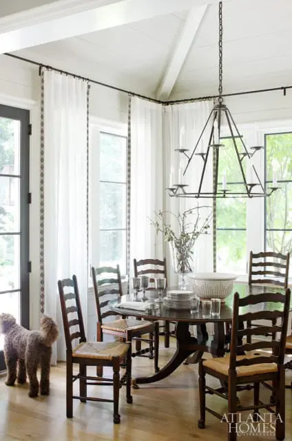 Dining room with dark wood oval table and ladder-back chairs with rush seats, set with plates and silverware. A large metal chandelier hangs overhead.