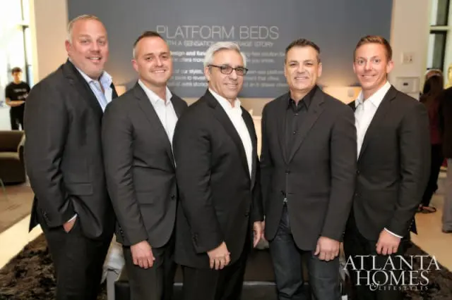 Five men in suits stand together in front of a wall with text that reads "PLATFORM BEDS WITH A SENSATIONAL STORAGE STORY". The Atlanta Homes & Lifestyles logo is visible in the lower right corner.