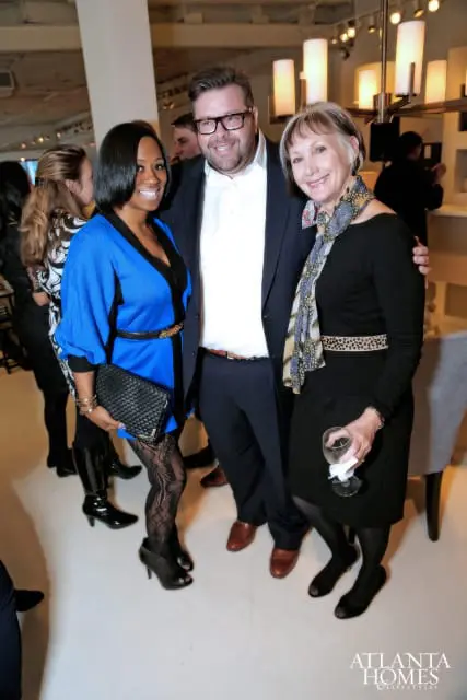 Three people posing for a photo at an event. A woman in a blue dress and black patterned tights is on the left, a man in a suit is in the middle, and a woman in a black dress and patterned scarf is on the right.