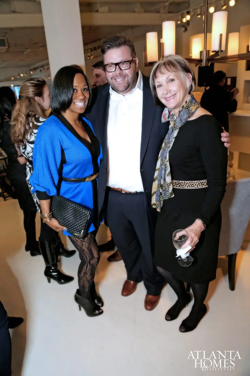 Three people posing for a photo at an event. A woman in a blue dress and black patterned tights is on the left, a man in a suit is in the middle, and a woman in a black dress and patterned scarf is on the right.