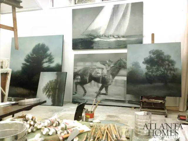 Artist studio with paintings of a sailboat, a jockey on a horse, and trees. Tubes of paint and brushes are scattered on the floor.