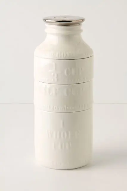 Stack of white ceramic measuring cups shaped like a milk bottle, with embossed markings for 1/3 cup, 1/2 cup, and 1 whole cup.