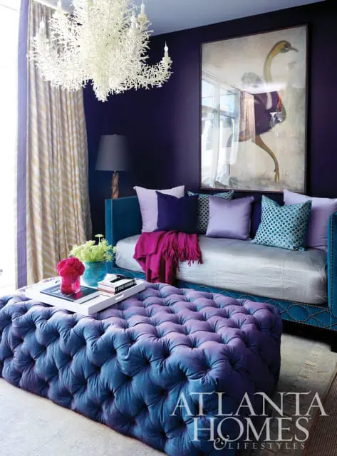 Purple living room with a teal daybed, tufted ottoman, and a large painting of an ostrich