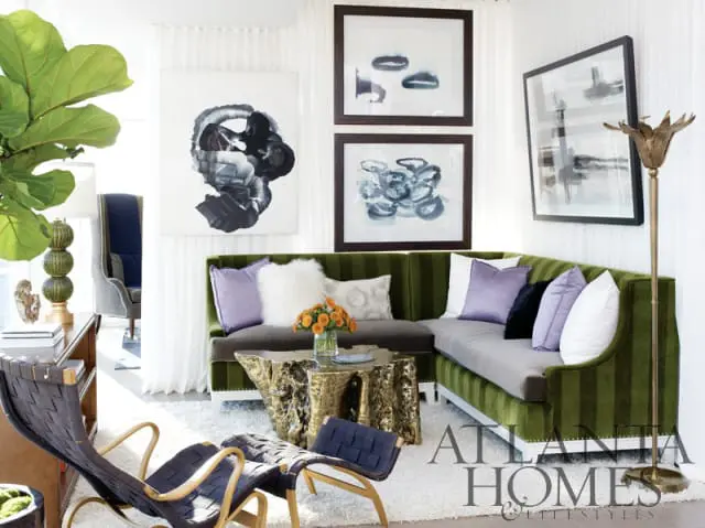 Living room with a green striped sectional sofa, gold abstract coffee table, dark woven chairs, and abstract art on the walls.